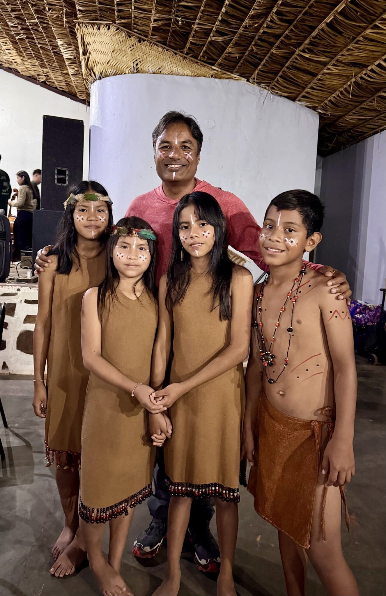 Man with traditional face paint posing with four Pemon indigenous children in ceremonial dress Canaima