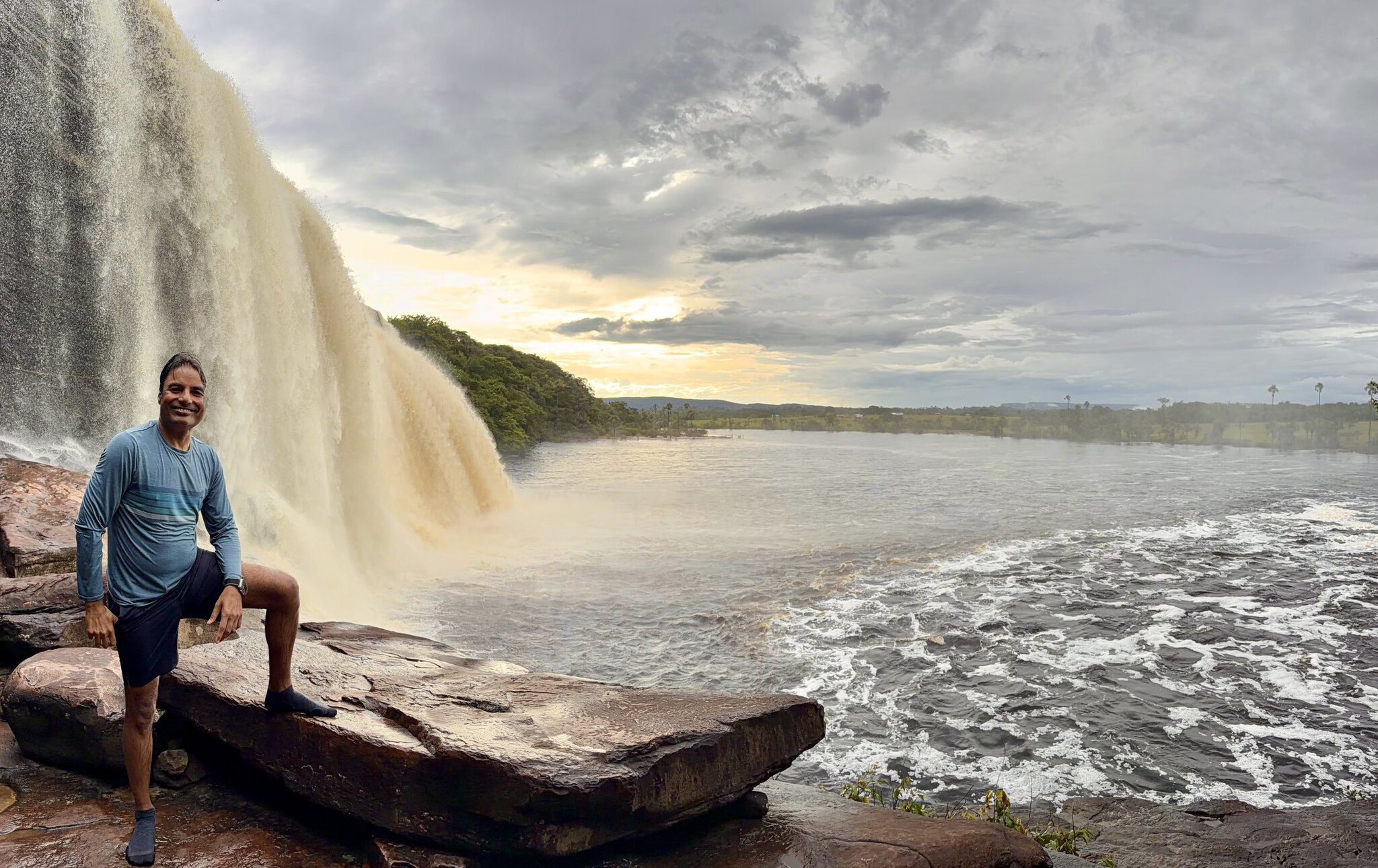 Man posing on rock beside massive Salto Hacha waterfall at Canaima lagoon during golden sunset