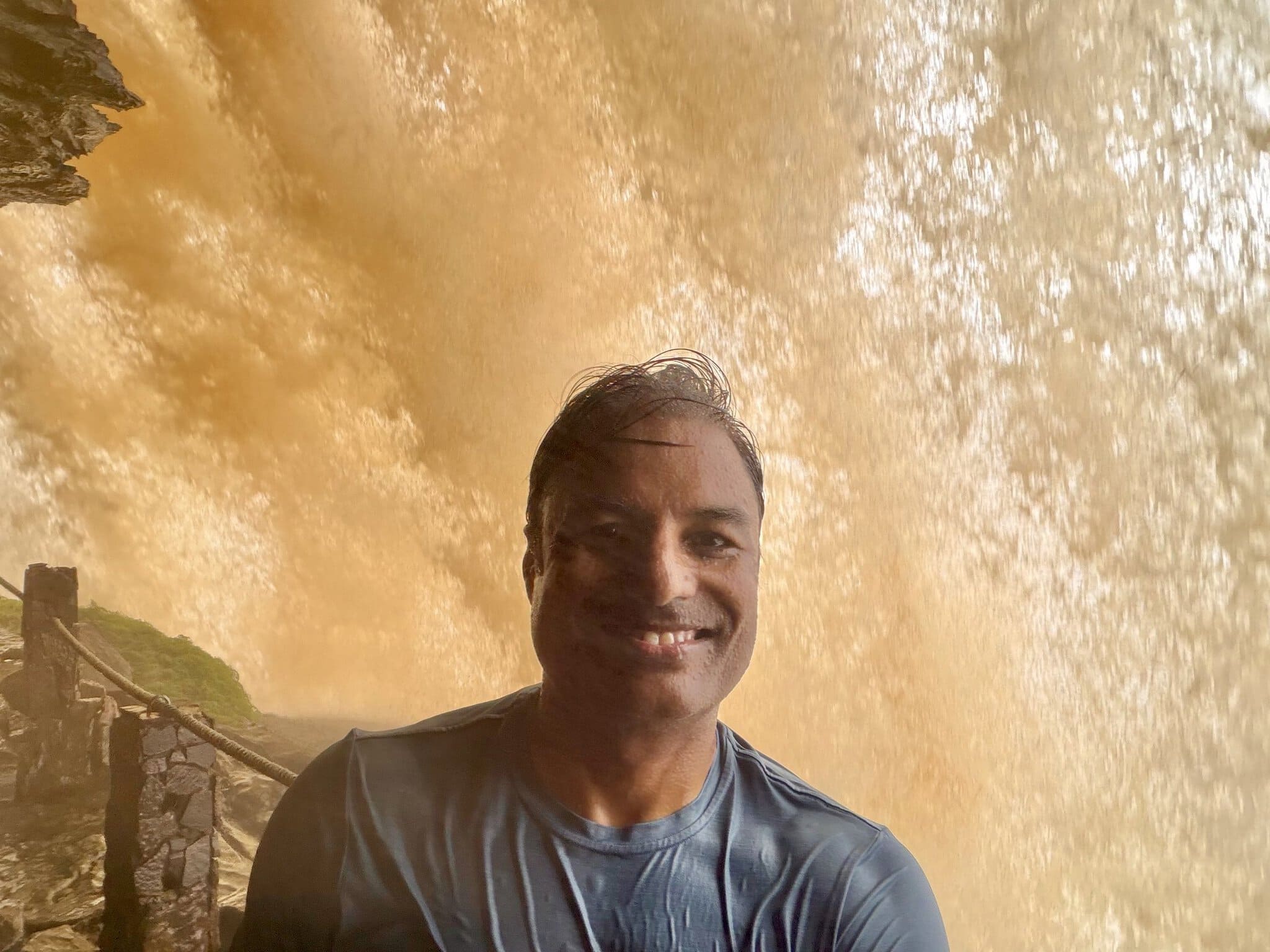 Man smiling soaking wet with golden orange waterfall roaring behind him at Salto Hacha Venezuela