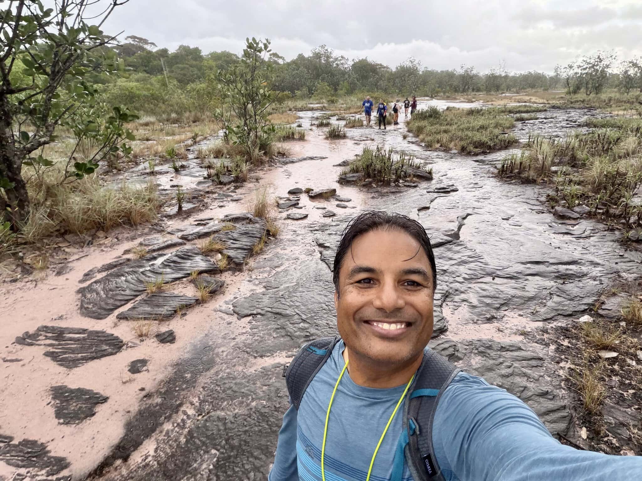 Smiling man taking selfie on ancient wet rock trail with trekking group behind him