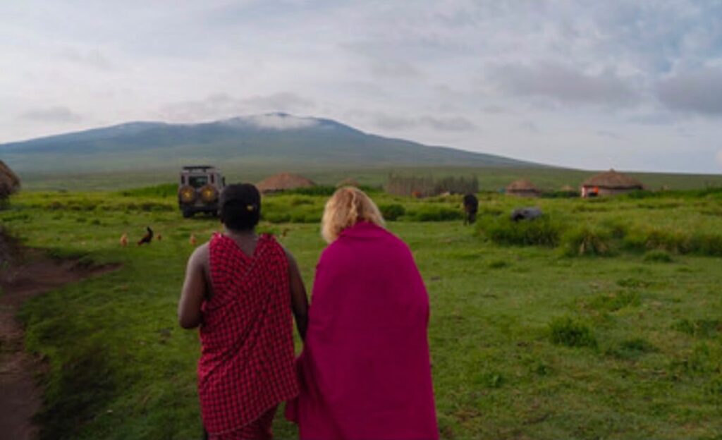 Two people walk toward a cluster of traditional Maasai homes in Ngorongoro at dusk